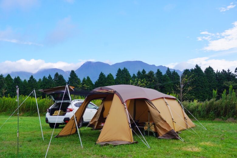 キャンプサイトに設営されたキャンビン型テントとテント横に駐車された白いSUV車