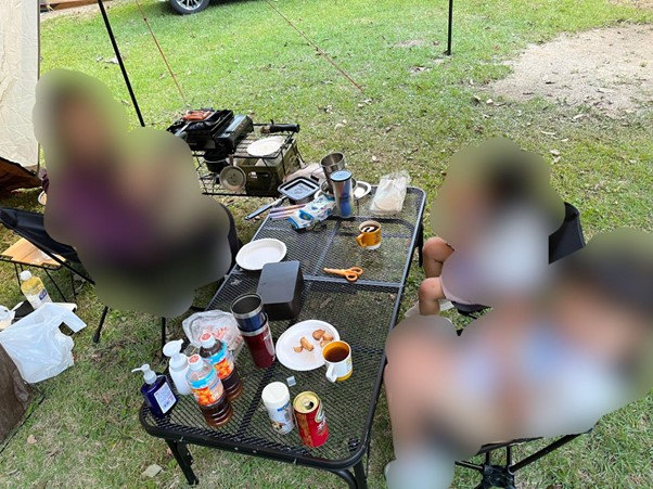 キャンプ場でタープの下でテーブルを囲い寛ぐ家族