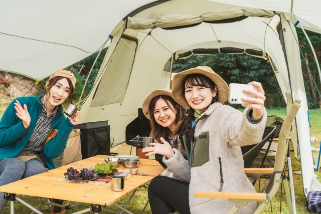 キャンプサイトでコーヒーを飲みながら写真を撮る三人の女性